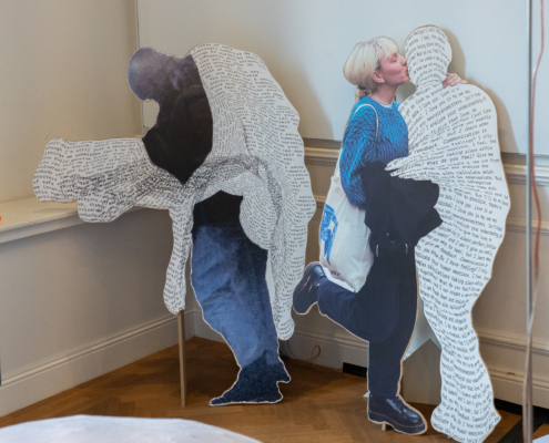Papierskulpturen mit Menschen, die Figuren aus Text umarmen und küssen